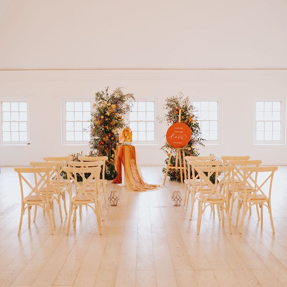 Golden wedding ceremony at Core Clapton Events wedding venue with wooden chairs, orange wedding sign and column flower arrangements 