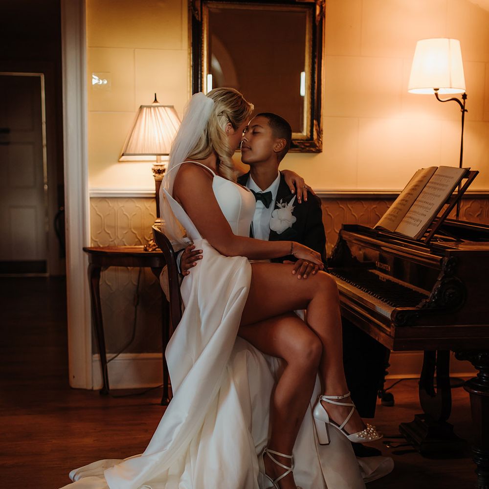 Bride in a side split wedding dress with pearl peep toe shoes sitting on her partners lap at a piano 
