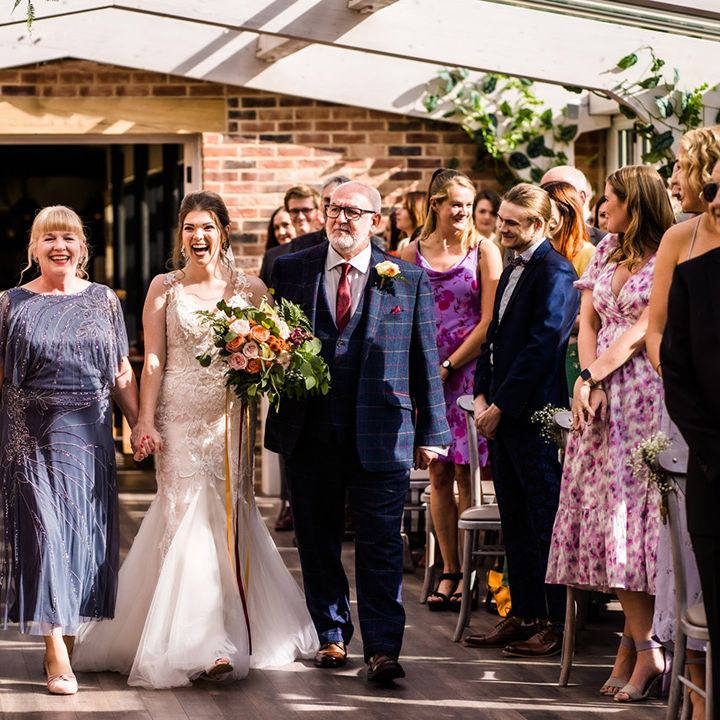 Bride in lace mermaid skirt wedding dress is walked down the aisle by her parents 