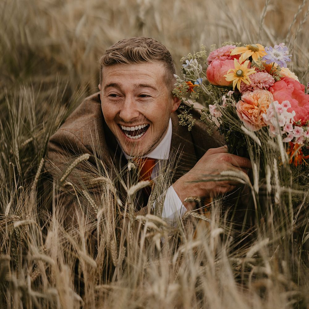 Groom is goofy in the fields posing with the bridal bouquet