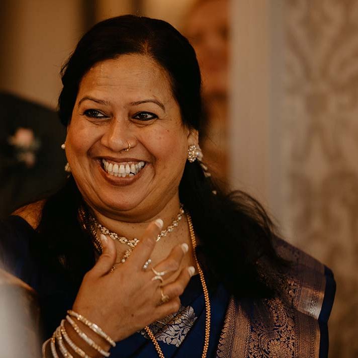 Happy guest at wedding in dark dress with gold embellishments and gold jewellery 