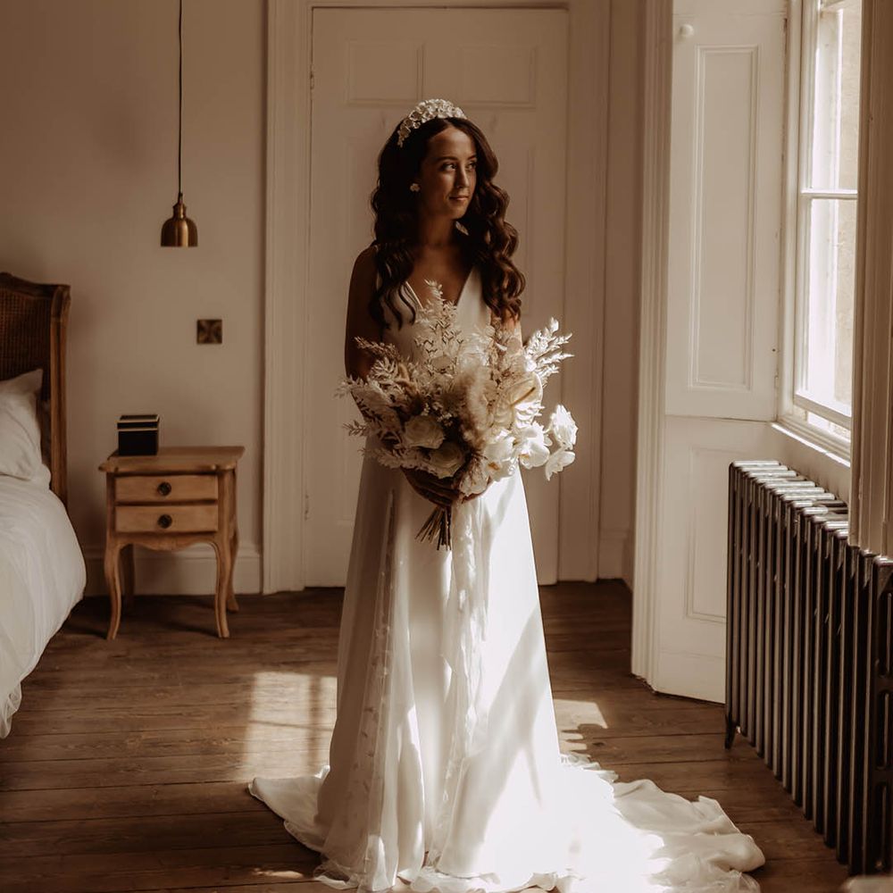 Bride with curled brown hair wearing a flower bridal headband and carrying a white orchid and dried flower wedding bouquet