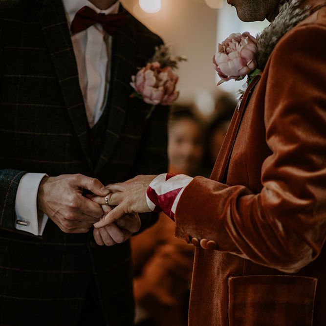 Groom places ring on his grooms hand during wedding ceremony 