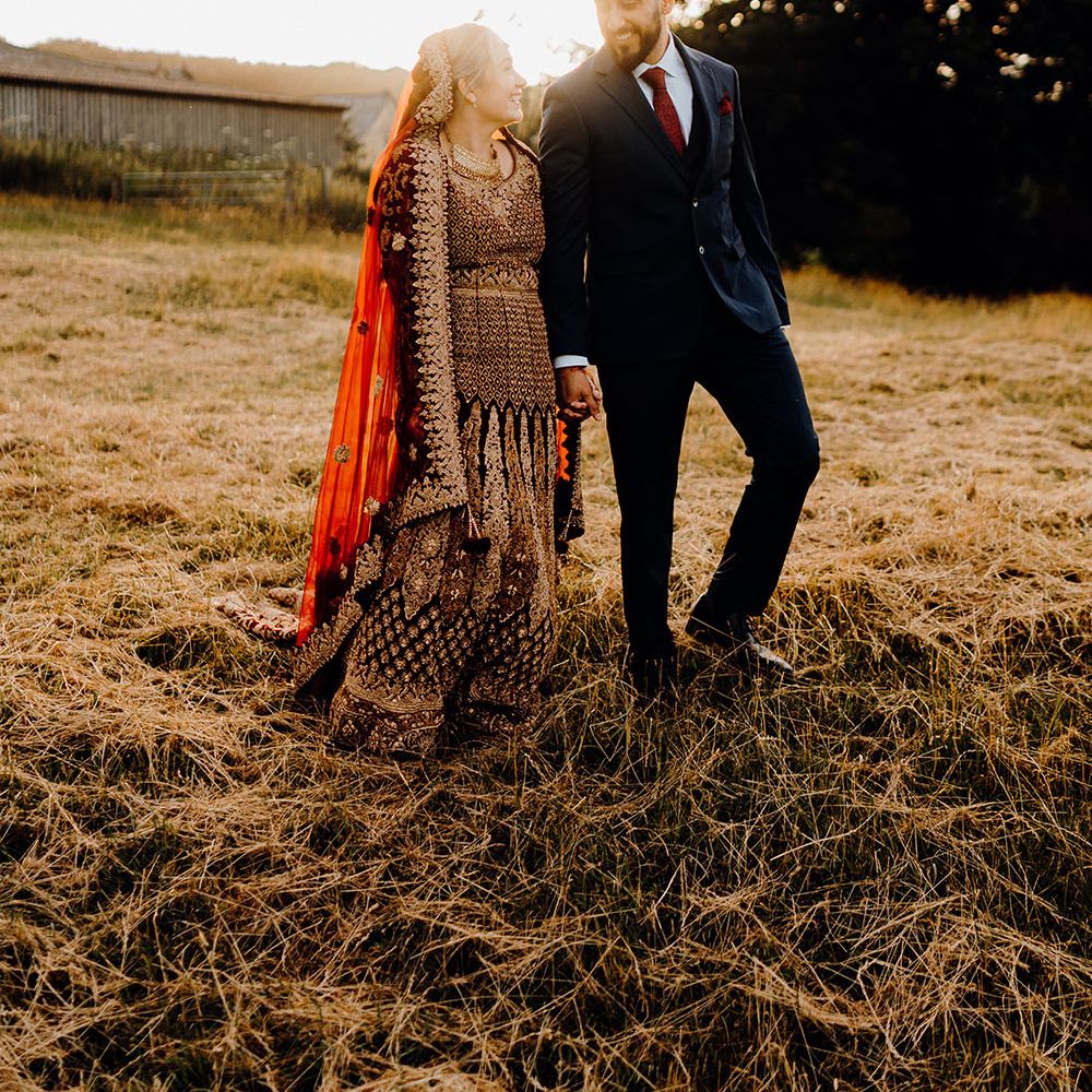 Bride & groom walk along fields during golden hour for multicultural wedding 