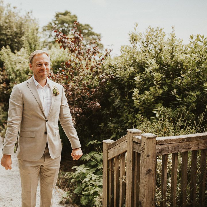 Guest in a pale wedding suit smiling as he gets the first look at the bride 