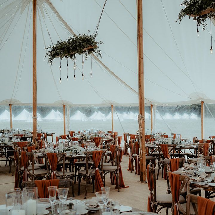 Marquee wedding reception with festoon lights and foliage with a burnt orange colour scheme, decorated chair backs and more