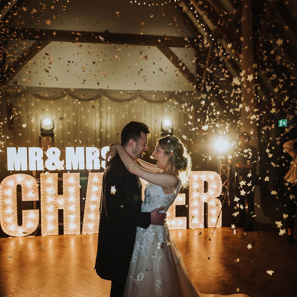 Bride and groom share their first dance in front of letter lights spelling out their new married name 