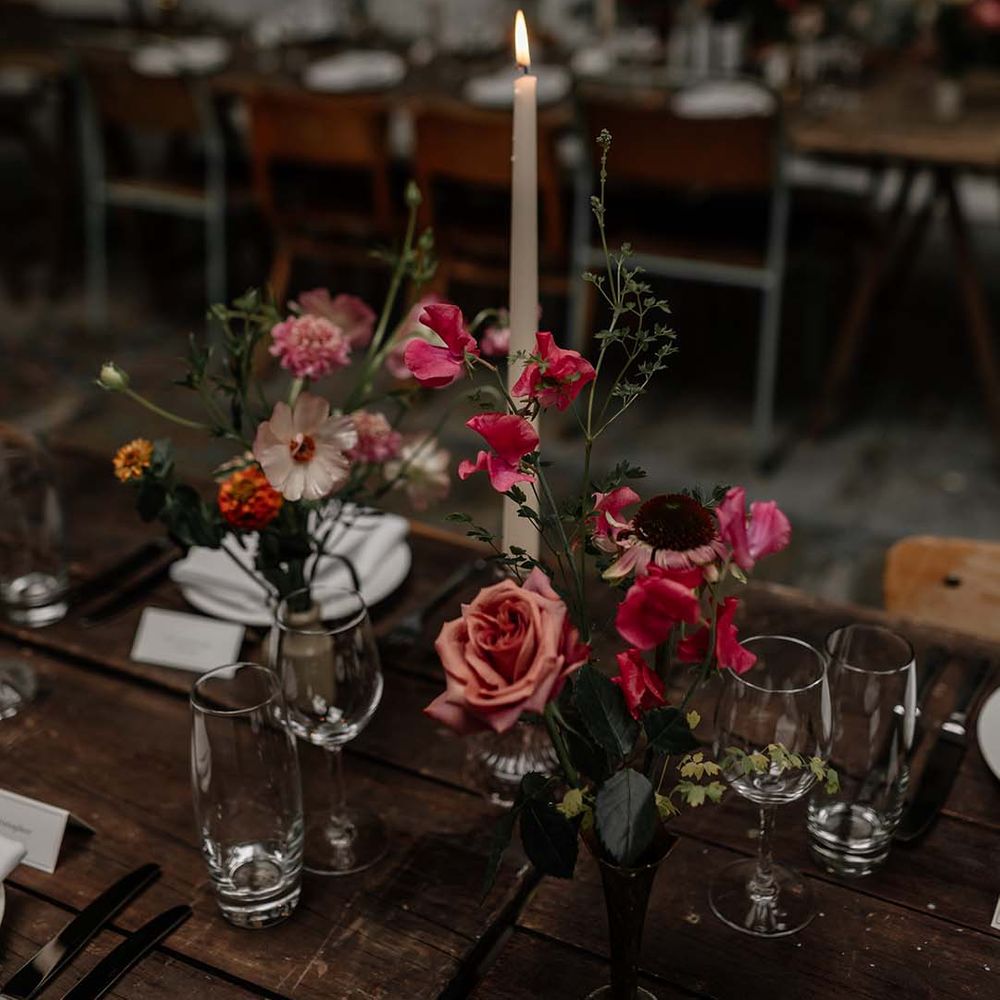 Long tapered ivory dinner candle in clear candle holder on minimal neutral wedding tablescape with pops of colourful floral decorations