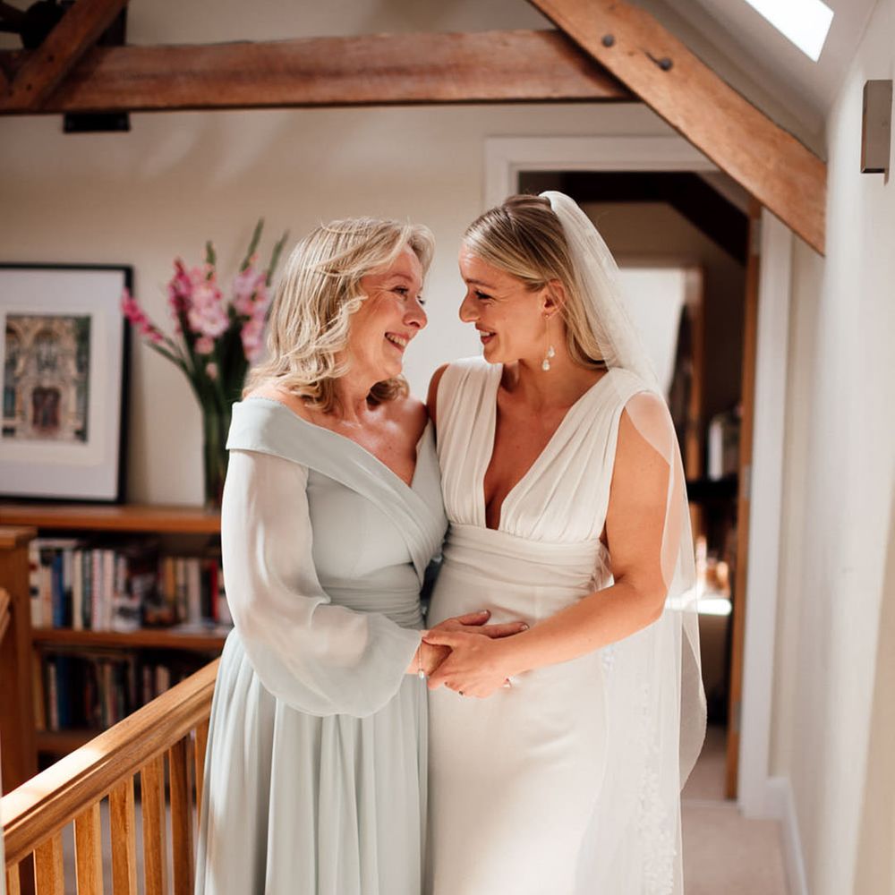 Mother of the bride in a sage green dress smiles at the bride as they get ready for the wedding 