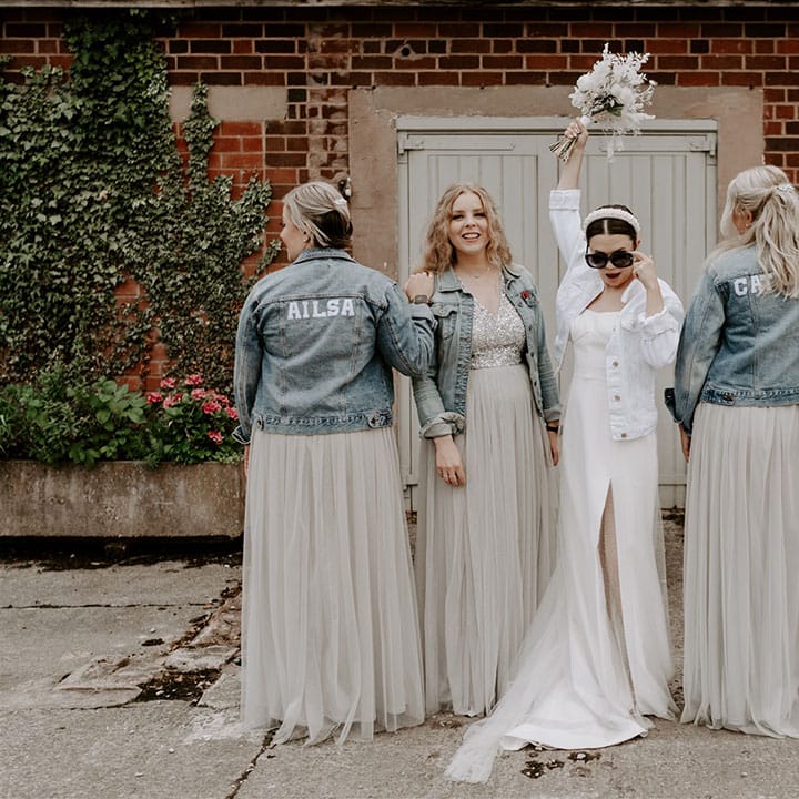 Bridesmaids wear customised light blue denim jackets with the bride in a white denim jacket, pearl headband and black sunglasses 