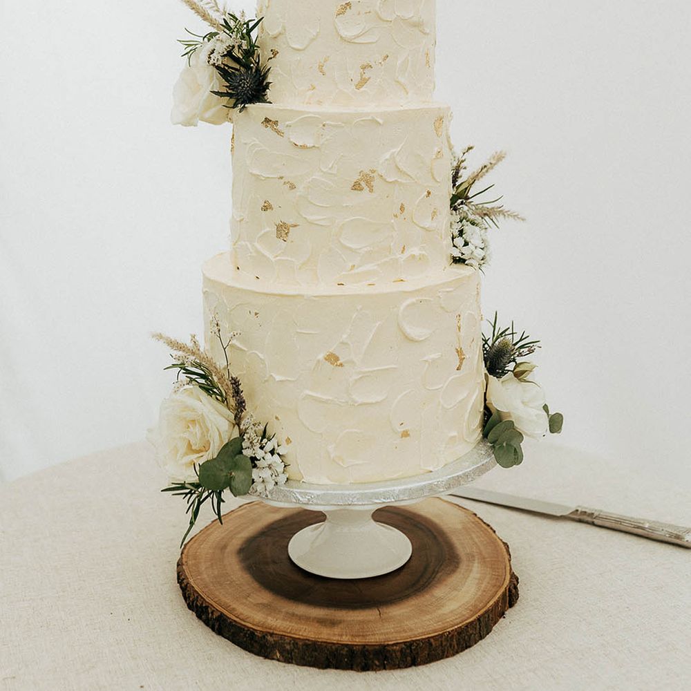 Three tier white frosted wedding cake complete with gold leaf and floral decor 