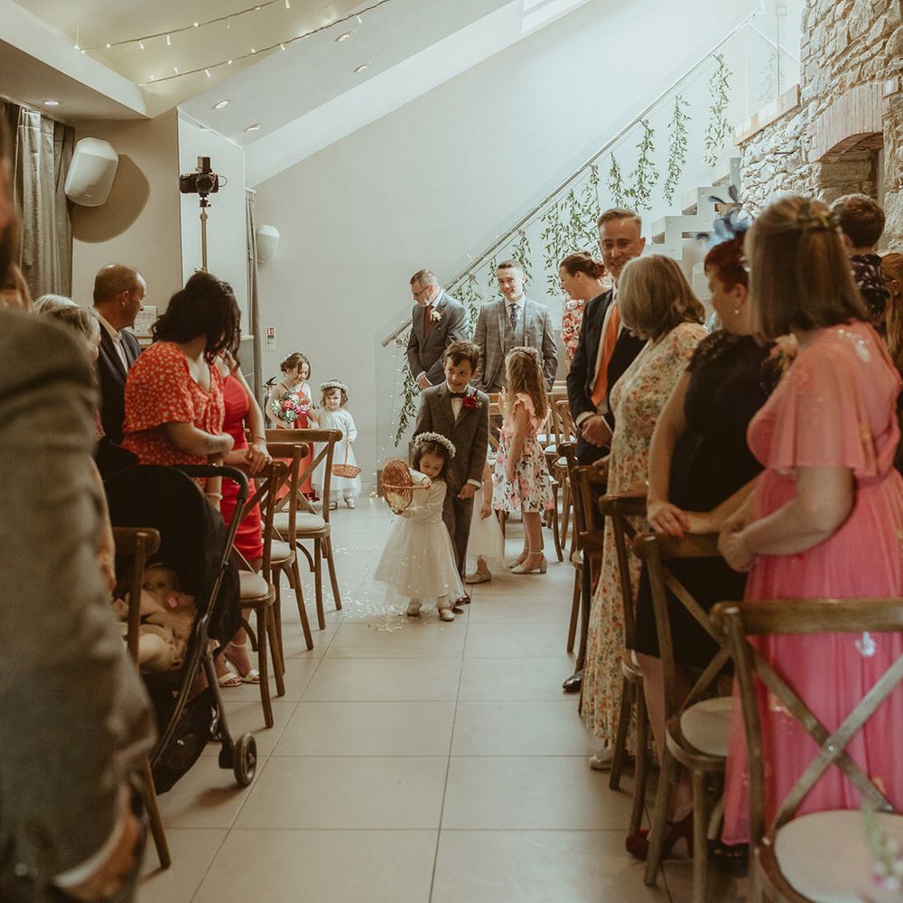 Wedding guests stand as the flower girl empties the wicker basket of white petals walking with other children a part of the wedding ceremony 