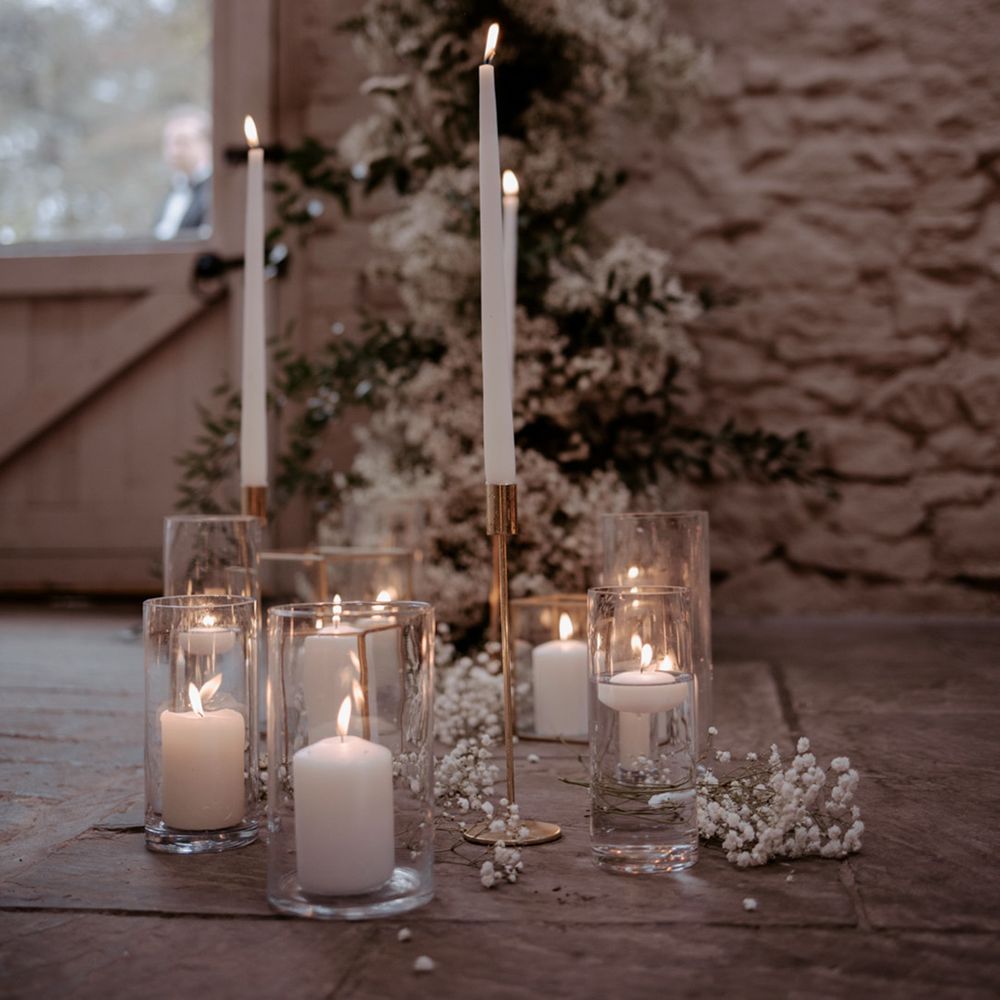 White pillar candles, floating tea lights and tall taper candles in glass candleholders decorate the aisle and altar for the wedding 
