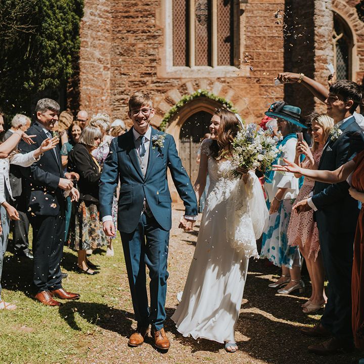 Groom in three piece navy and grey wedding suit having confetti moment with the bride in a traditional lace wedding dress 