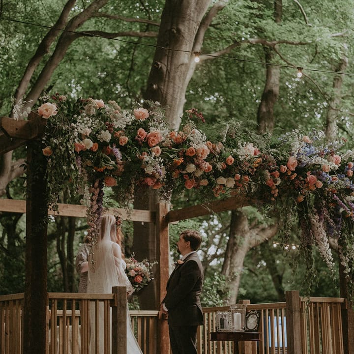 Outdoor woodland wedding with colourful pink, purple and white wedding flower altar decoration 