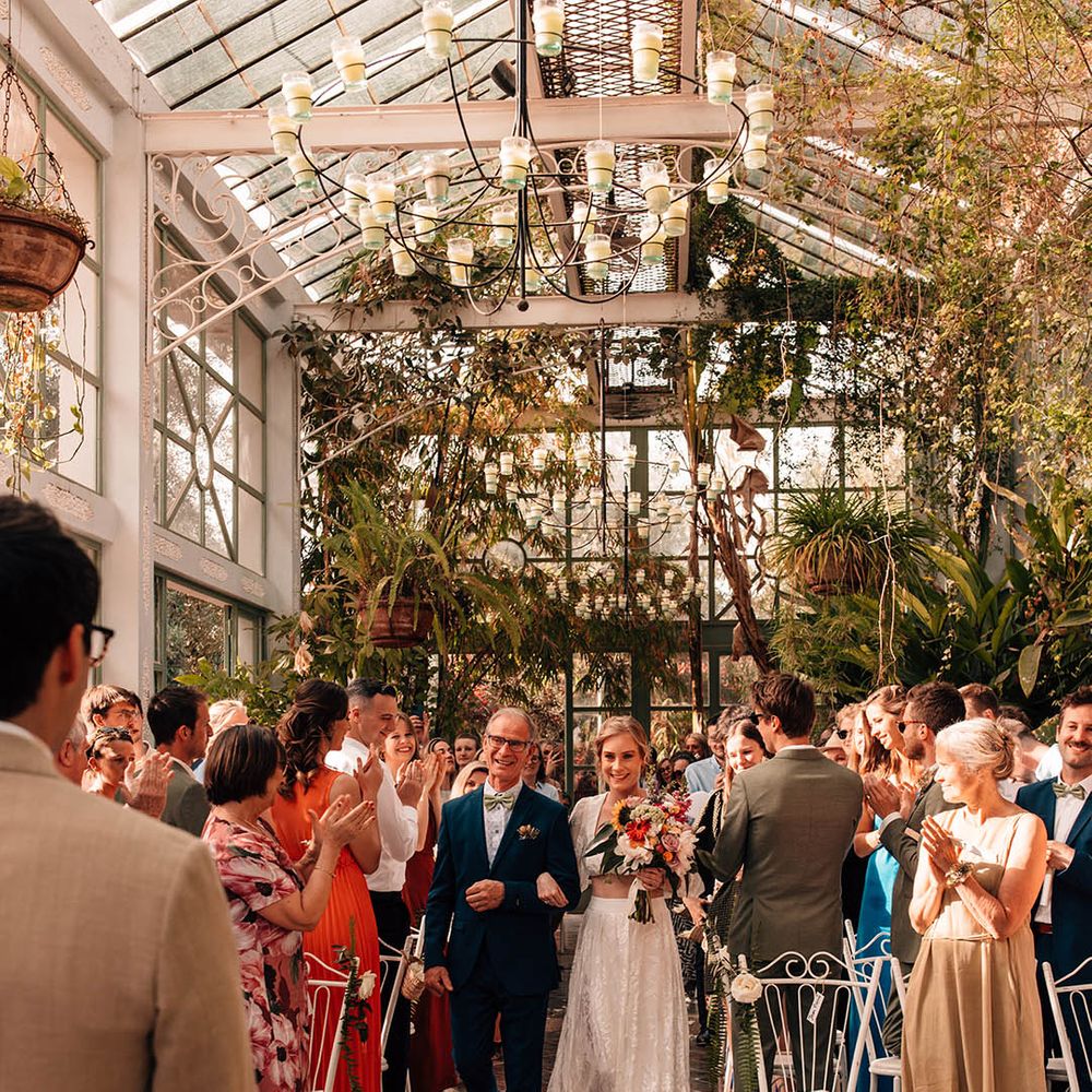 Bride in modern two piece carrying a colourful bouquet with sunflowers walking down the aisle with her father 