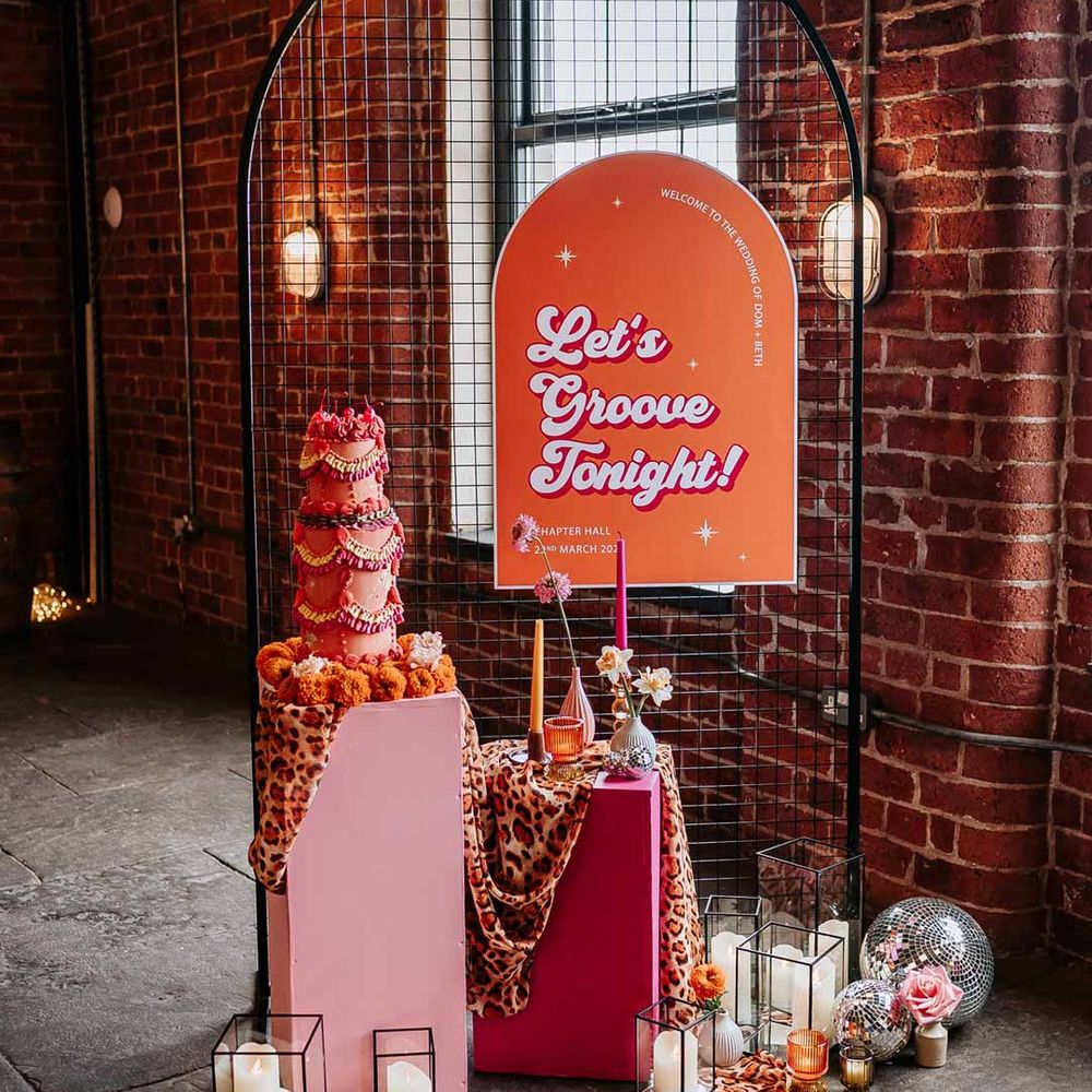 Retro wedding inspiration - large orange and pink retro wedding sign, retro wedding cake, leopard print wedding drapes, pillar candles and disco ball wedding decor 
