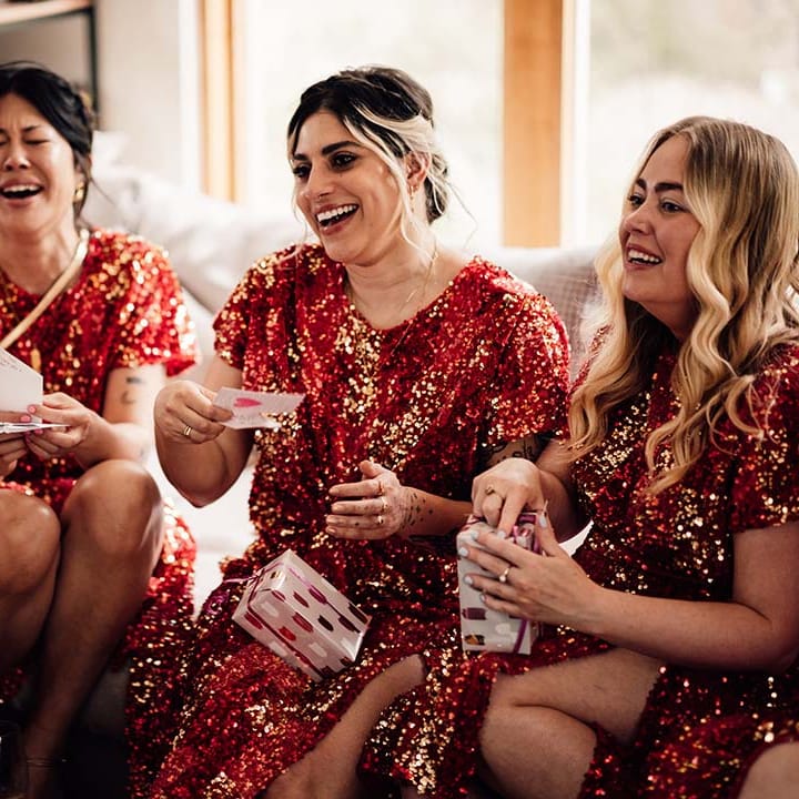 Bridesmaids getting ready for the wedding and opening presents in red sequin bridesmaid dresses 