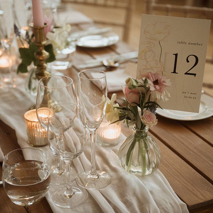 Pretty floral table number sign with small pink bud vases with draped table runner and pink wedding candles 