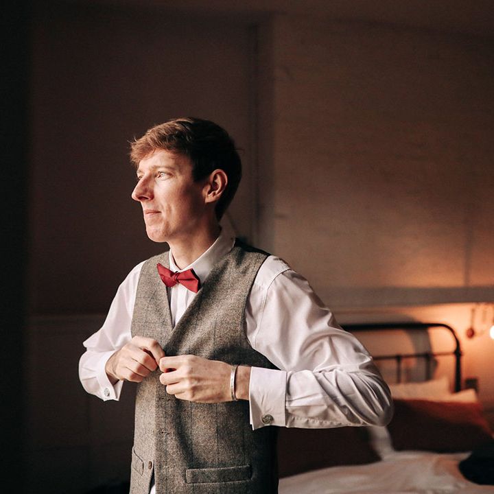 Groom wearing grey waistcoat with red bow tie getting ready for the wedding day