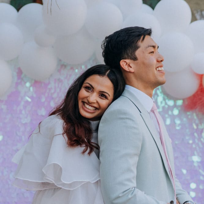 Bride in short wedding dress embracing her groom in pale green suit 