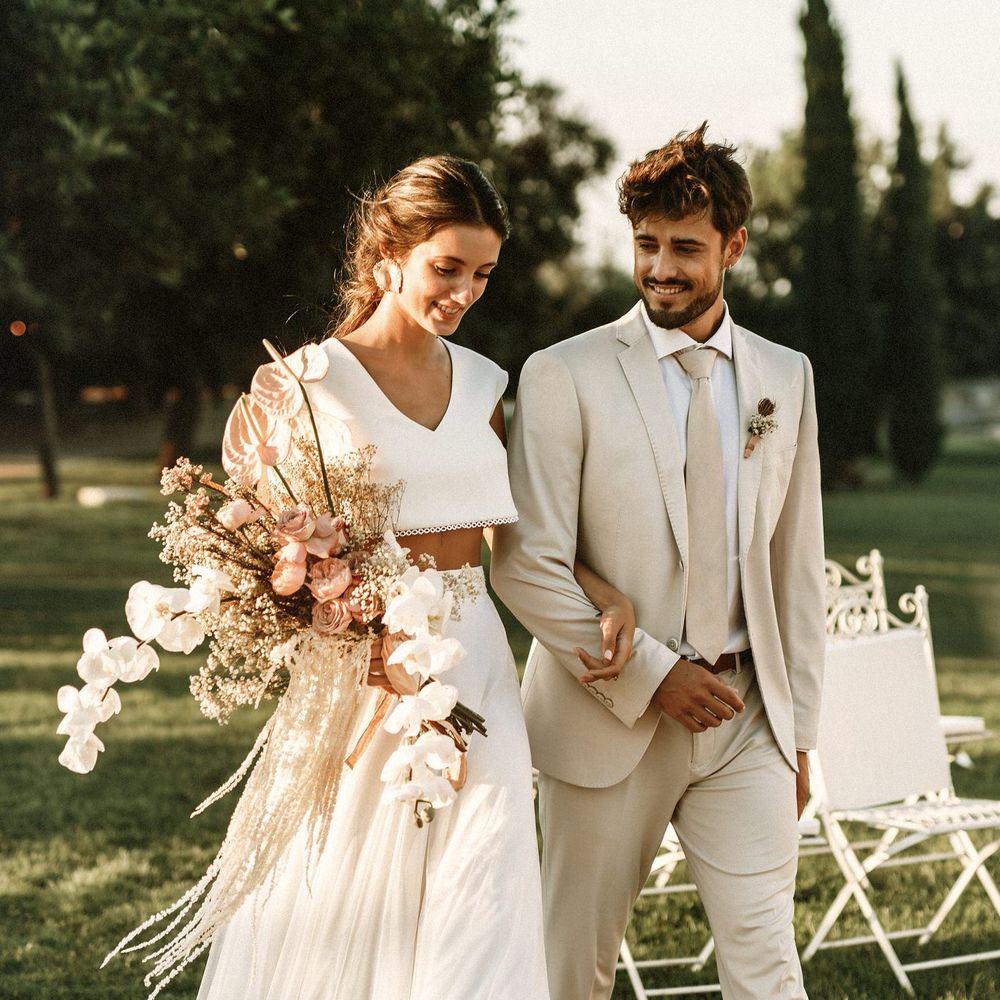 Boho bride in separates holding an orchid bouquet walking down the aisle with her groom in a beige suit 