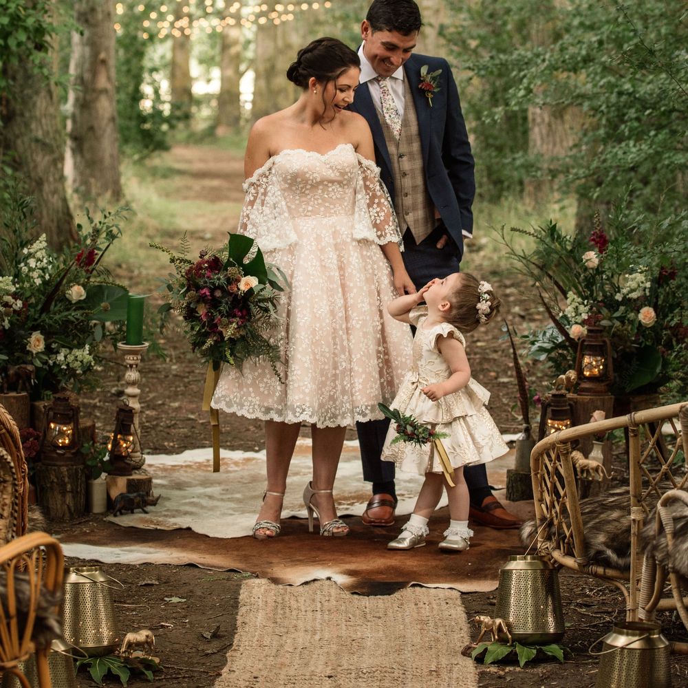 Bride & groom stand under trees with little girl surrounded by lights