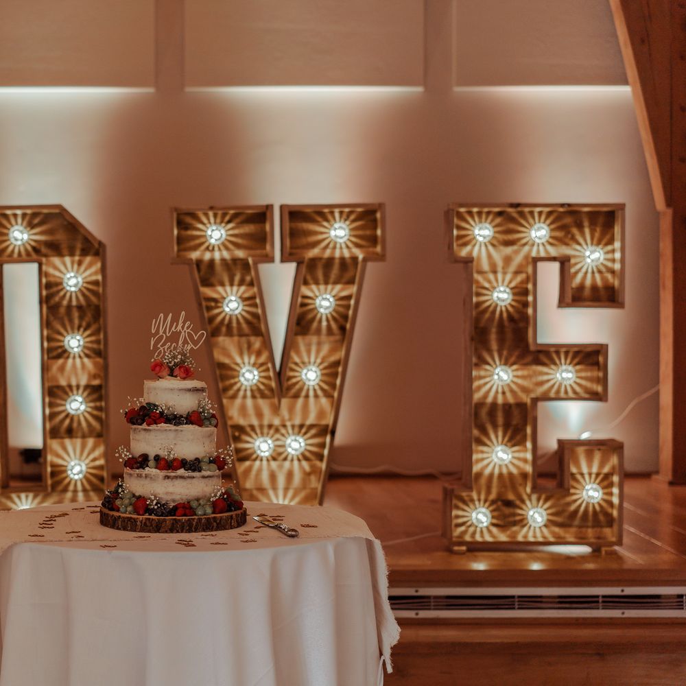 Lit up LOVE wedding sign sits behind naked wedding cake with fruit decor