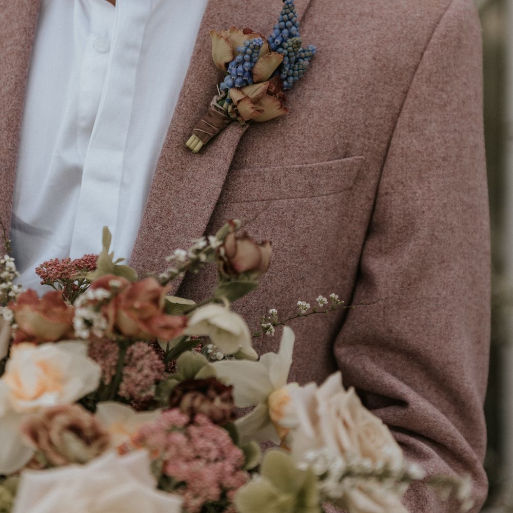 Groom wears pastel pink suit with white shirt and pastel blue floral buttonhole 