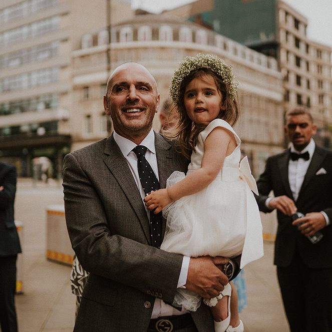 Wedding guests holding the flower girl in a tulle skirt dress and flower crown 