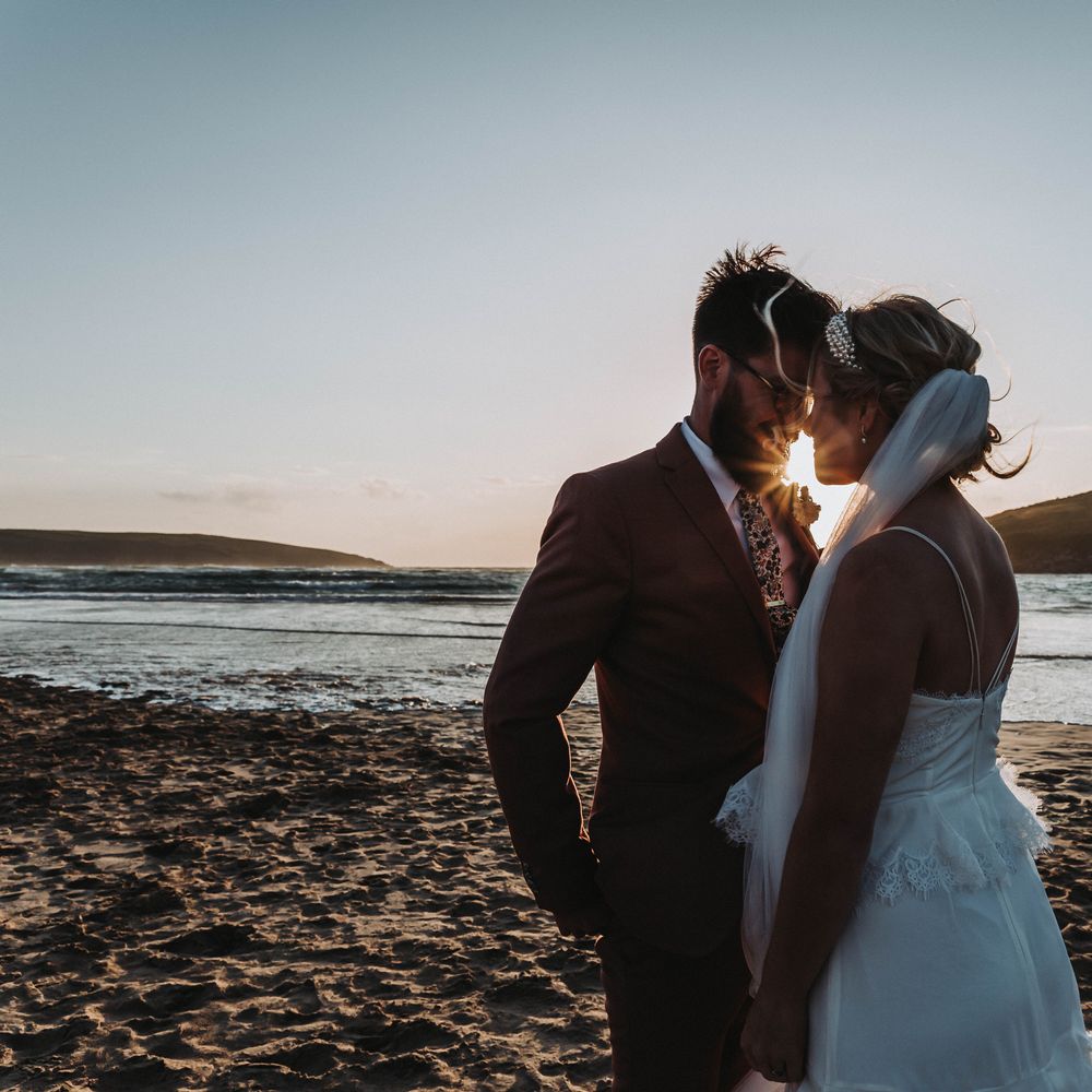 Bride & groom look lovingly at one another on the beach as the sun sets behind them