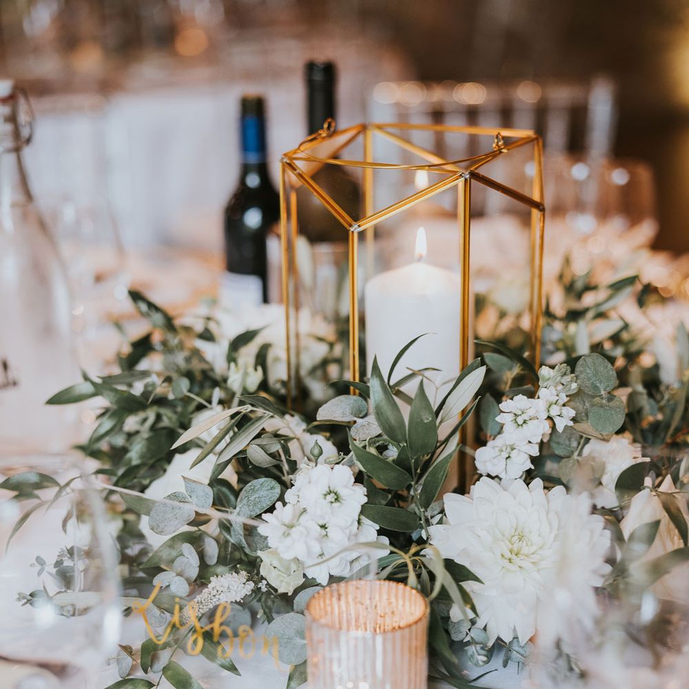 White and green floral centrepiece with candle in glass holder for elegant wedding table at Notley Abbey