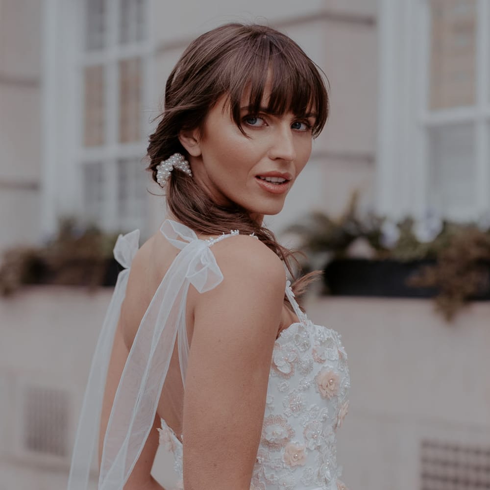 Bride with a fringe in a tea length wedding dress with appliqué flowers and ribbon straps 
