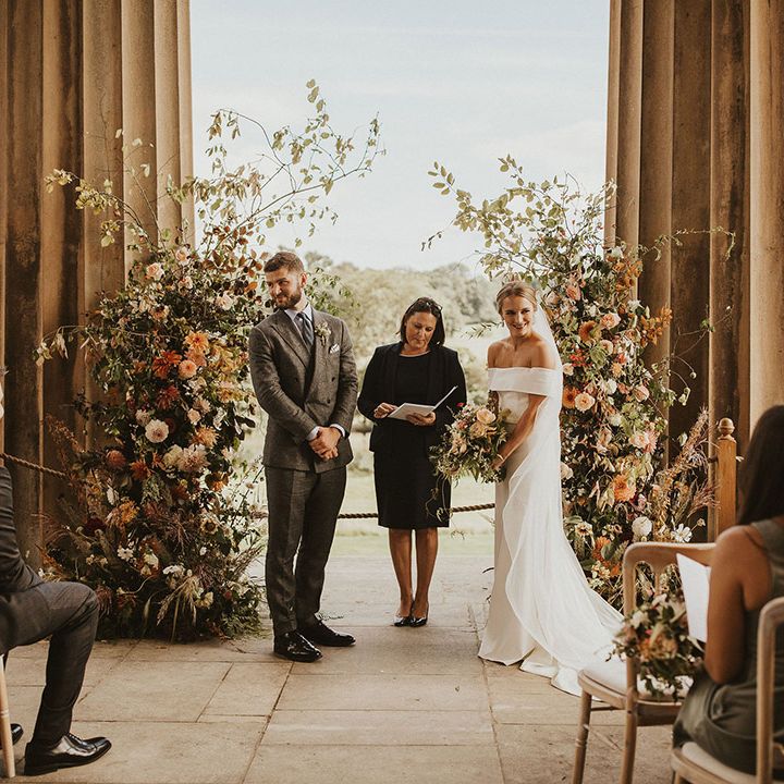 Bride & groom stand in front of floral archway on their wedding day during ceremony