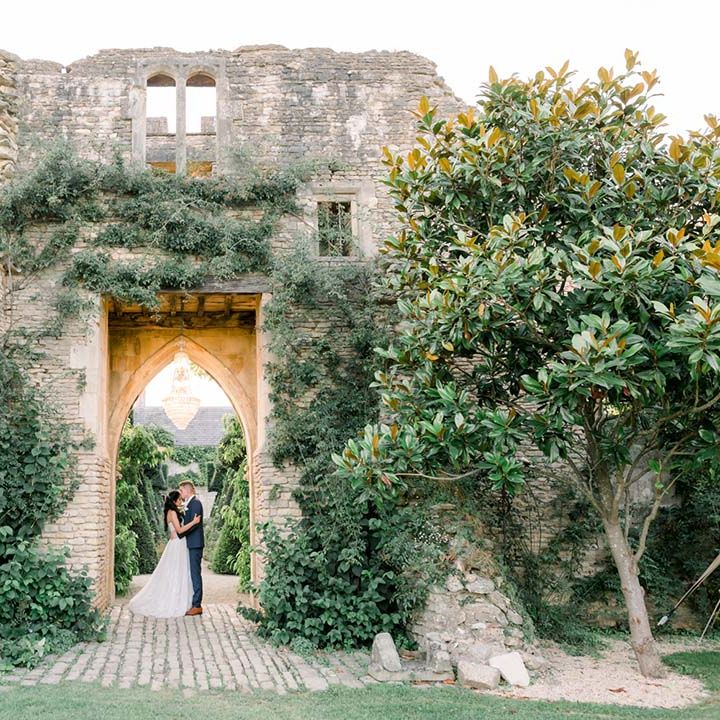 Bride & groom kiss under archway outdoors on their wedding day