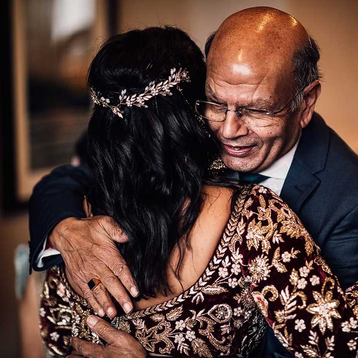 Hugs and smiles for the bride who wears flower hair piece in her dark loose curled hair 
