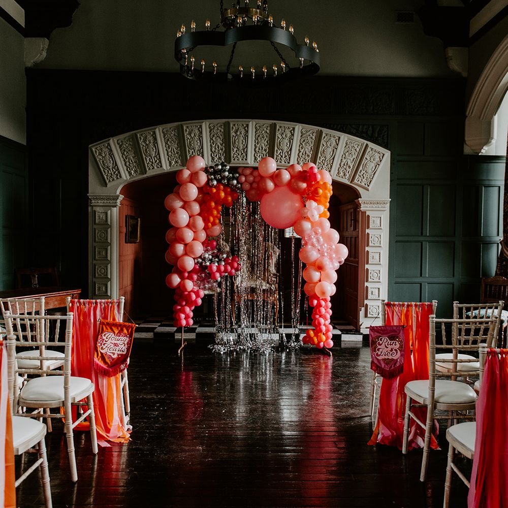 Highfield House wedding venue aisle wedding decor with vibrant red balloon installation, tinsel backdrop and banner chair backs 
