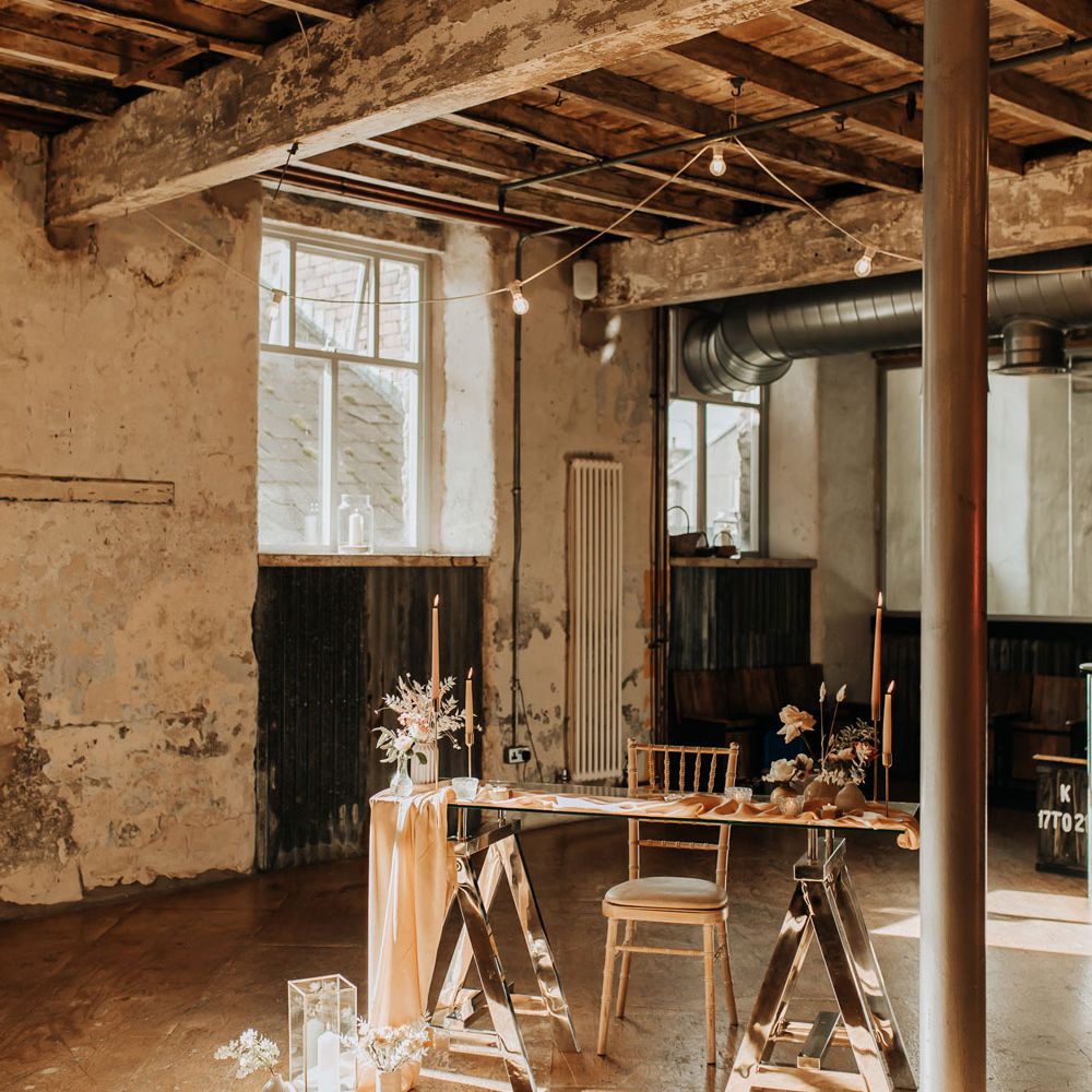 Glass wedding registry table with wooden chair, draping and candles at industrial wedding ceremony 