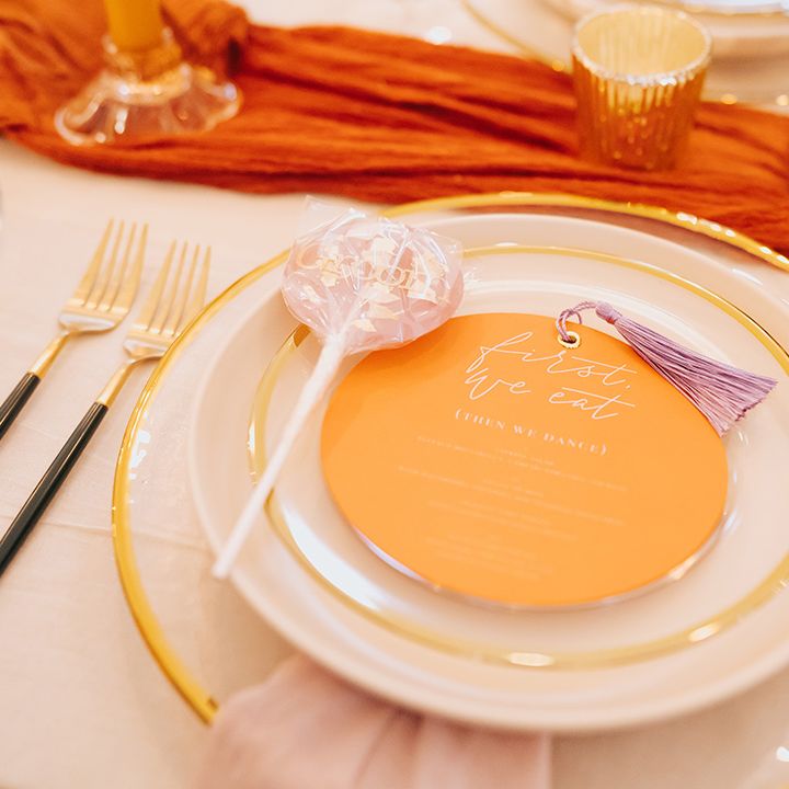 Gold rimmed charger plates with gold cutlery and orange menu card for elegant place setting 