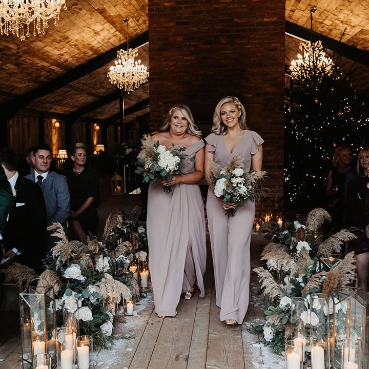 Two bridesmaids in taupe outfits walk down the aisle together for winter wedding at the Lake District