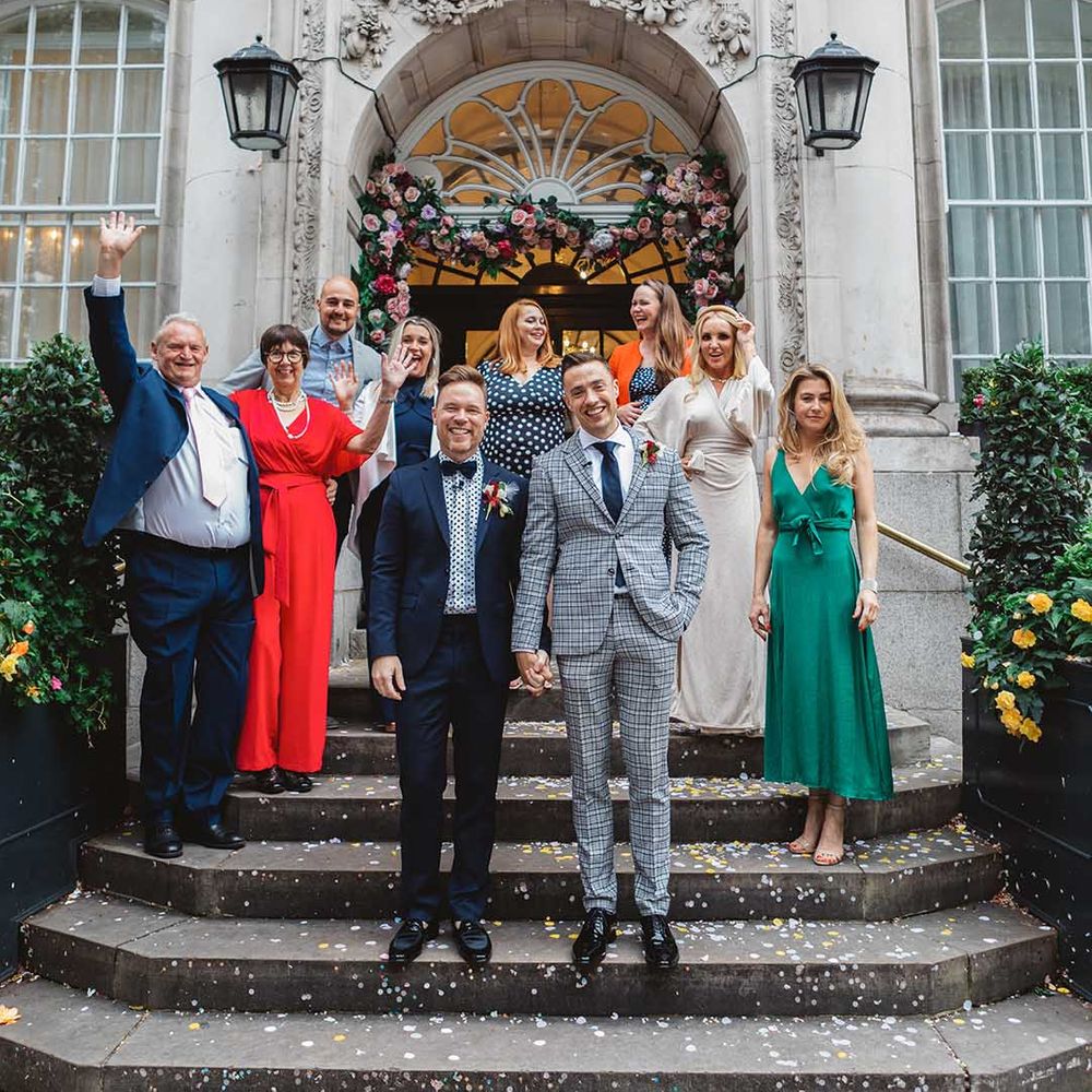 Grooms stand with their wedding guests outdoors on steps 