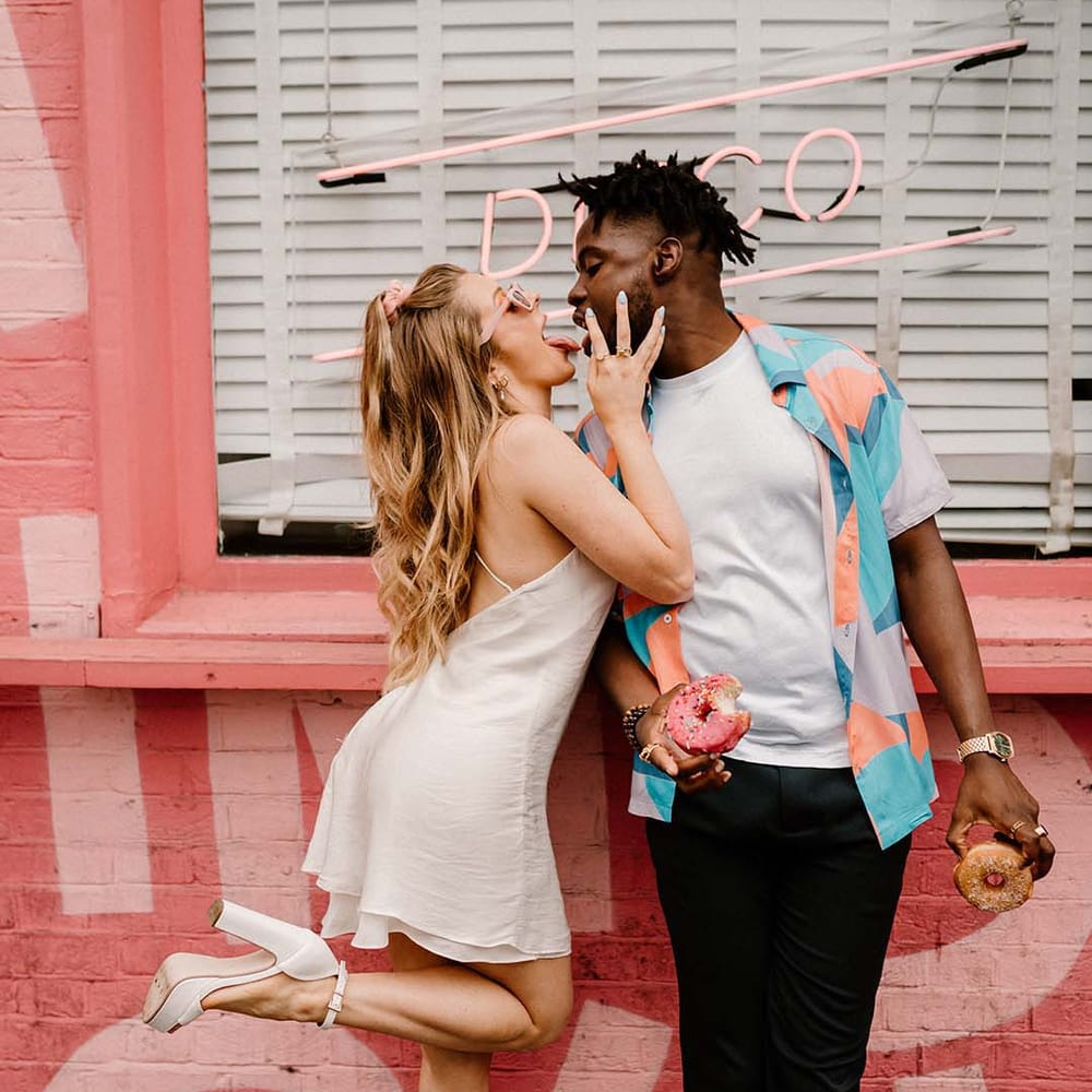 fun city elopement with bride in a short wedding dress and groom in a patterned shirt eating doughnuts 
