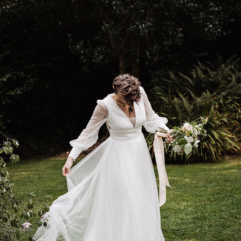 Bride in sheer long sleeved wedding dress with tulle skirt and pink and white bouquet