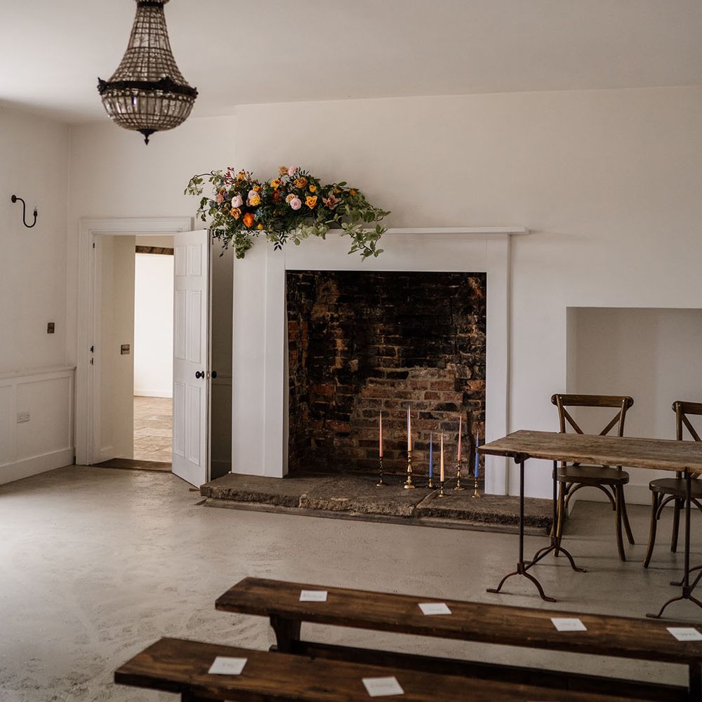Aswarby Rectory ceremony room with colourful taper candles in the fireplace with yellow, orange, pink and blue flowers 