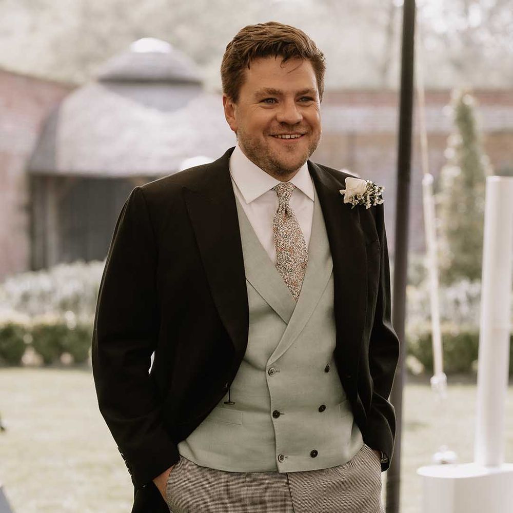 Groom smiles in black morning suit with puppytooth trousers, mint green waistcoat and patterned tie 