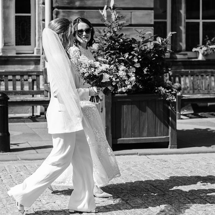 Brides walk along in black and white image on their wedding day in Edinburgh 