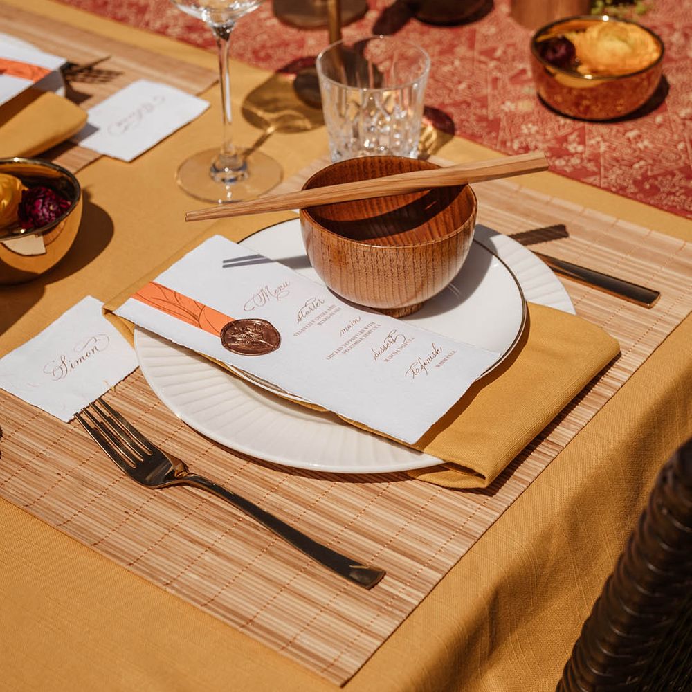 Tablescape with yellow table rubber, bamboo place mat, gold cutlery, brown rice bowls, wooden chopsticks, gold candlesticks and menus card for Japanese wedding 