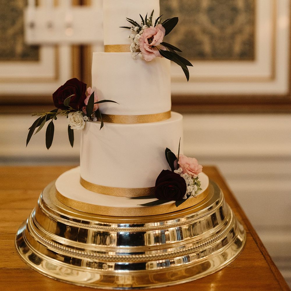 Three tier wedding cake complete with white icing, gold ribbon and floral decor 