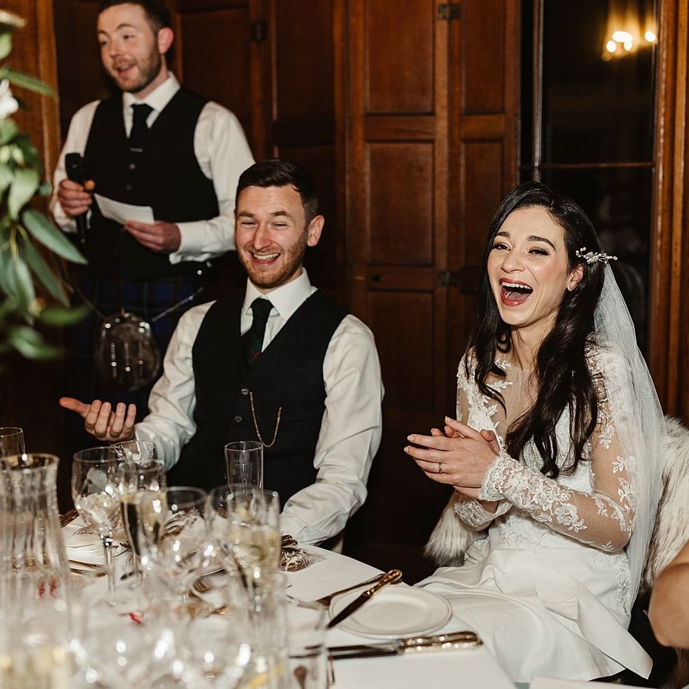 Bride & groom laugh during wedding reception speeches at Drumtochy Castle in Scotland for winter wedding