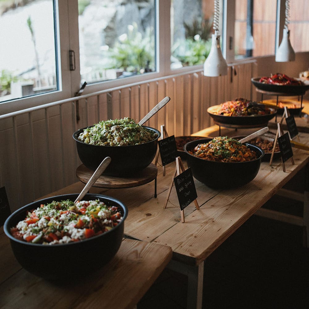 Wooden tables with buffet styled wedding breakfast in black bowls 